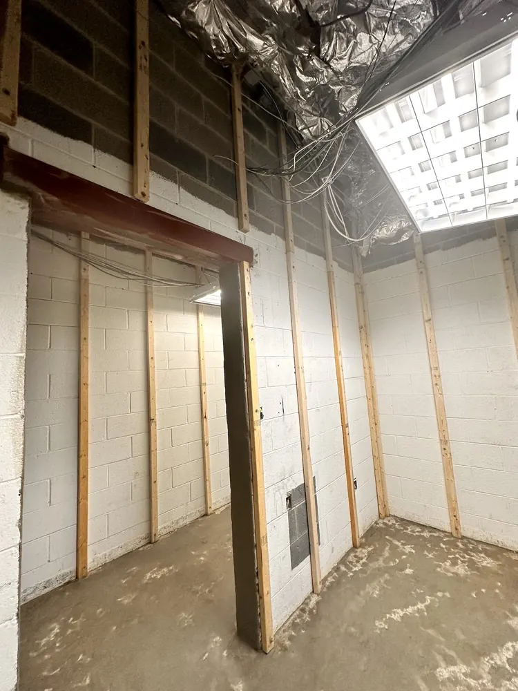 A block-walled room with wood furring and a new steel-framed opening.