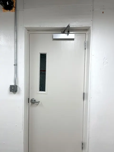 A finished white door with closer and vision panel.