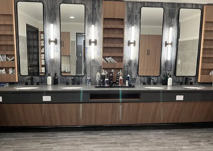 Finished vanity wall at Woodmont Country Club: tall lit mirrors on grey stone above wood casework.